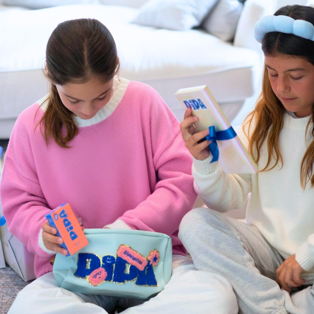Pipa Pouch in light blue with gold glitter chenille patches holding skincare products next to two girls sitting on the floor