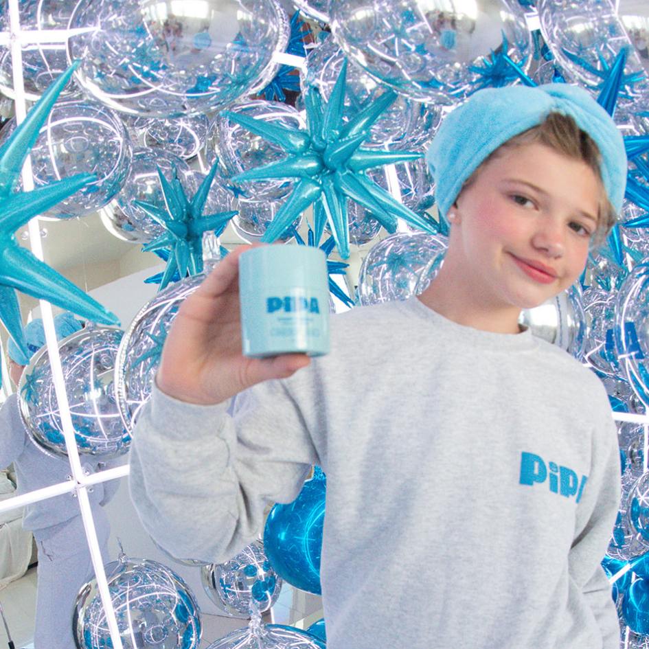 Tween wearing Pipa Hair Towel in blue microfiber with matching sweatshirt holding Pipa product against shiny blue and silver balloon backdrop