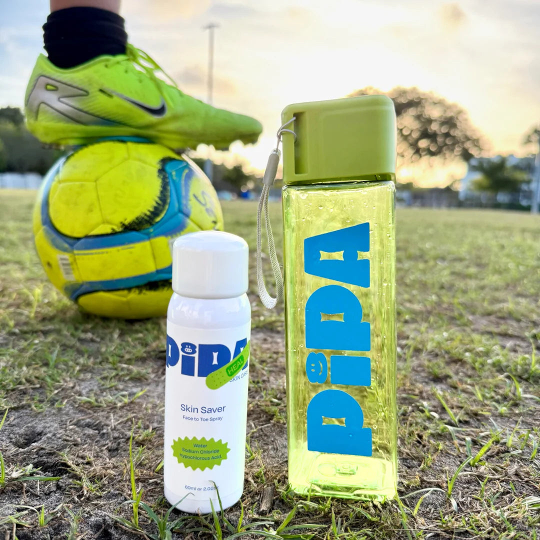 Skin Saver Duo with face and body spray and Pipa Water Bottle on grass field with soccer ball and shoes in background.