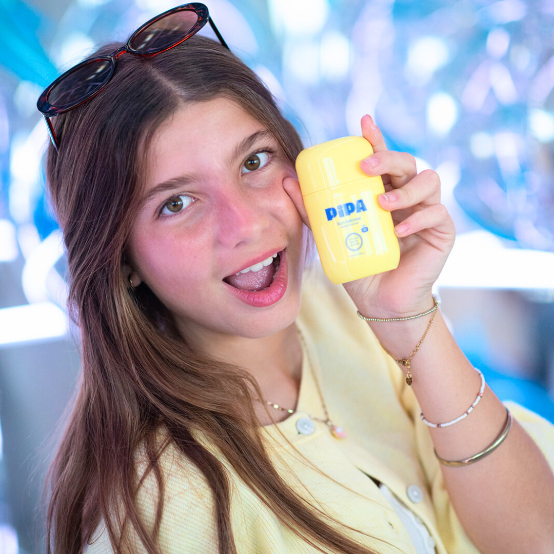 Young woman holding yellow Sun-Sational SPF 30 mineral sunscreen for glowing skin protection